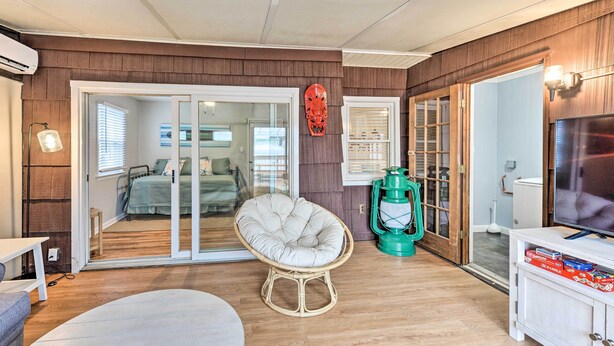 Una sala de estar acogedora con un sillón de mimbre, un televisor y una puerta corrediza de vidrio que da a un dormitorio.
