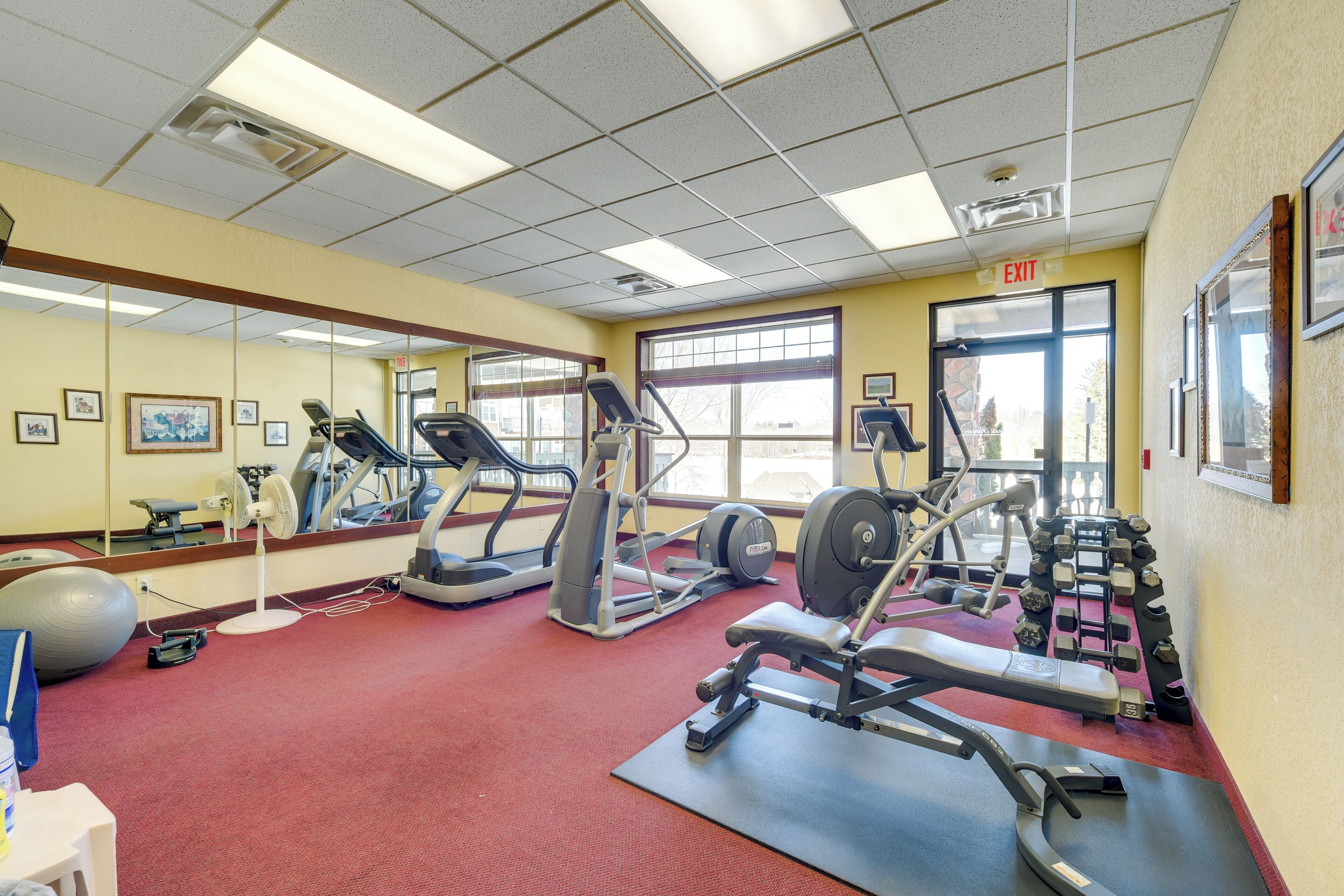 A gym with exercise equipment, a mirror, and a red carpeted floor.