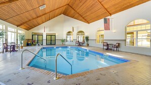 Una piscina interior con vigas de madera en el techo, suelo de baldosas y vistas al exterior a través de amplias ventanas.