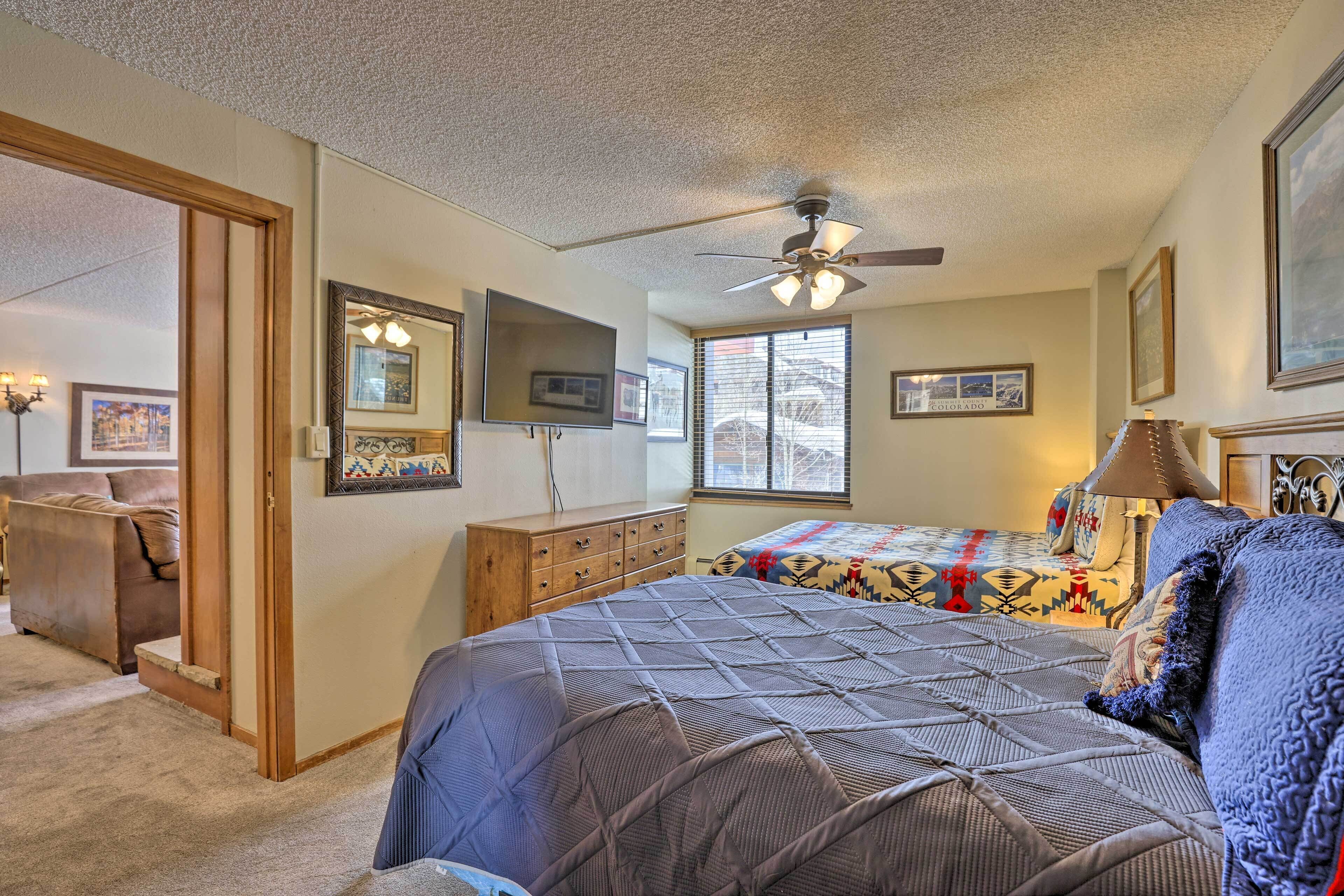 A bedroom with a bed, a ceiling fan, a dresser, a window, and a door leading to another room.
