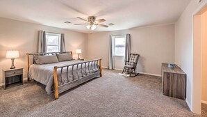 Une chambre à coucher comprenant un lit, des tables de chevet, une chaise, un bureau et un ventilateur de plafond.