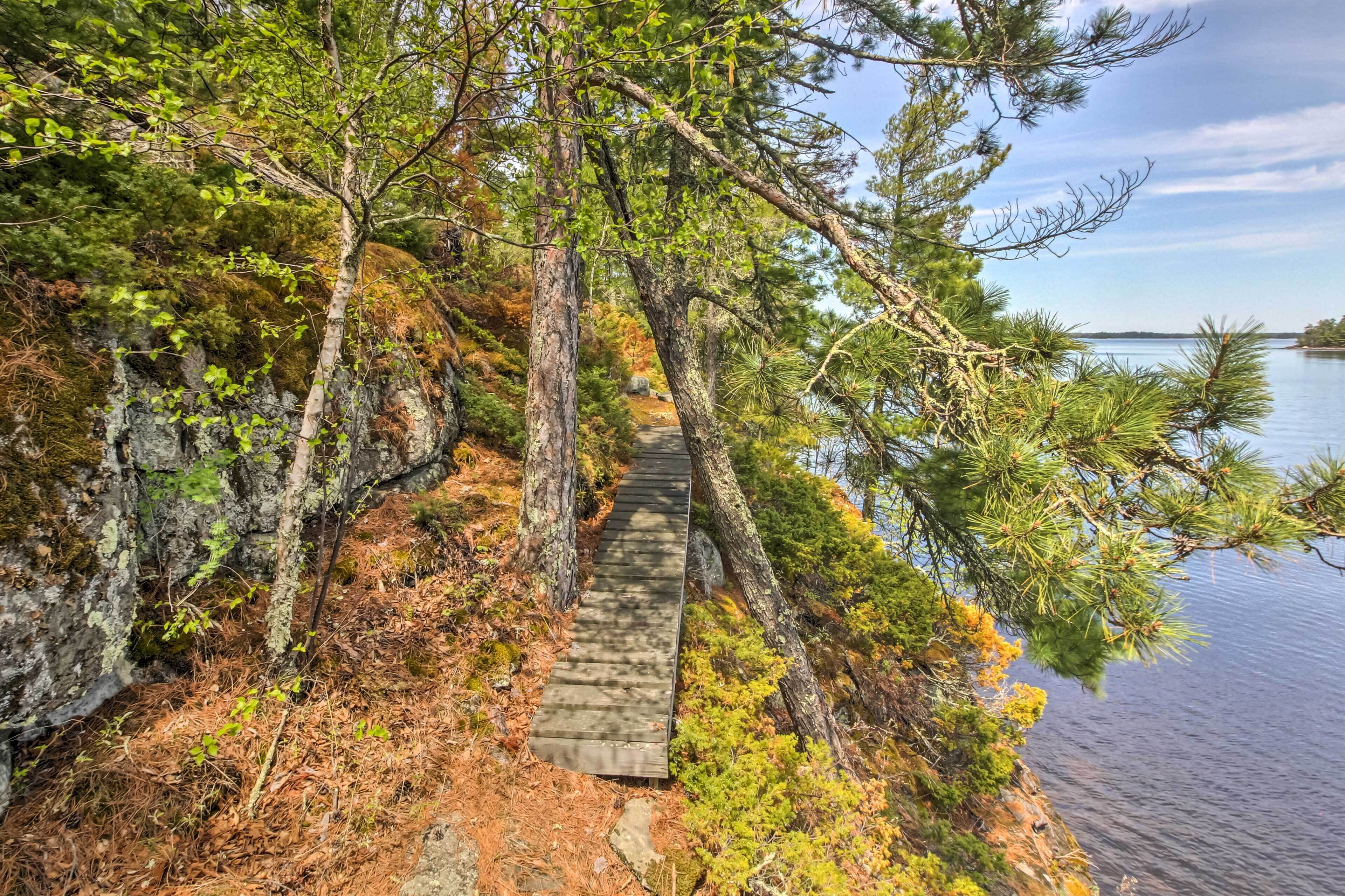 A wooden boardwalk leading to a lake surrounded by trees and rocky terrain.