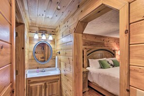 A wooden cabin interior with a wooden bed, a round mirror, a sink, and a nightstand. - Charming Mtn Cabin 2 Mi From Downtown Boone! (Boone)