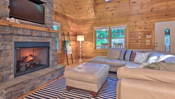 A cozy cabin interior with a stone fireplace, wooden walls, a sofa, and a patterned rug. - Charming Mtn Cabin 2 Mi From Downtown Boone! (Boone)