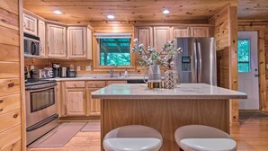 A wooden cabin-style kitchen with a central island, stainless steel appliances, and two bar stools. - Charming Mtn Cabin 2 Mi From Downtown Boone! (Boone)