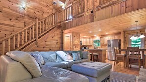 A spacious living area with a large L-shaped sectional sofa, wooden staircase, and a kitchen area with modern appliances. - Charming Mtn Cabin 2 Mi From Downtown Boone! (Boone)