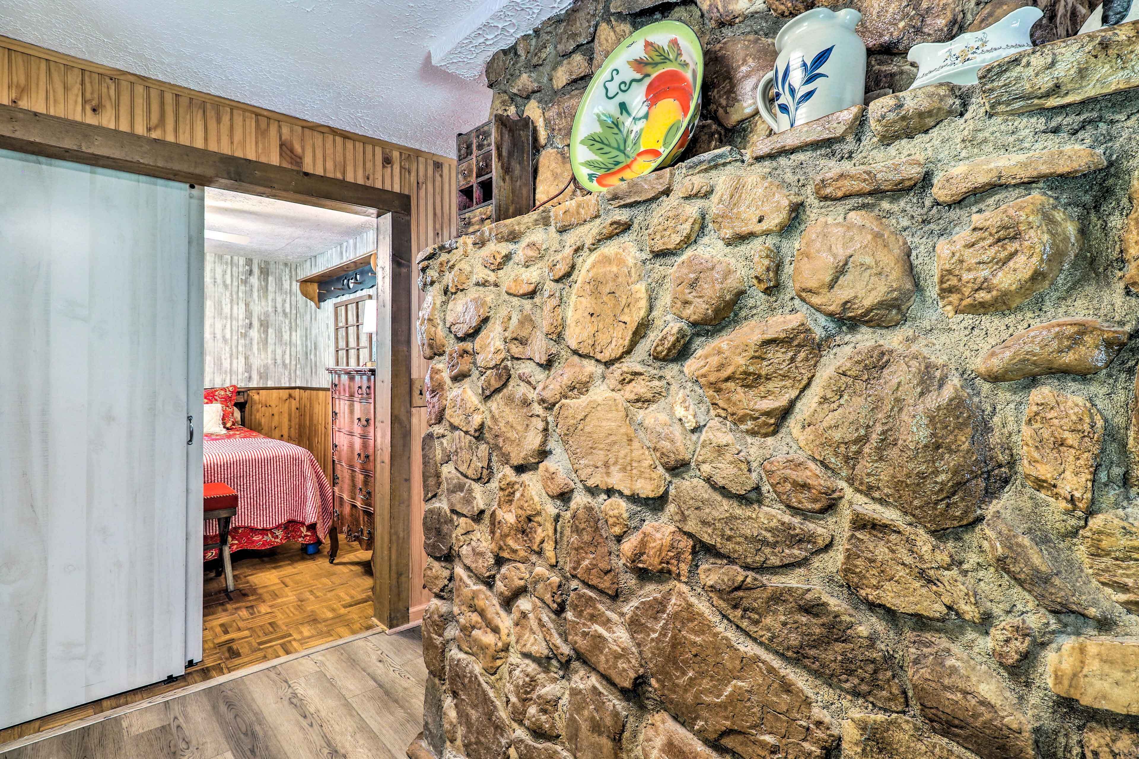 A rustic room with a stone wall, wooden door, and a bed with a red and white checkered bedspread.