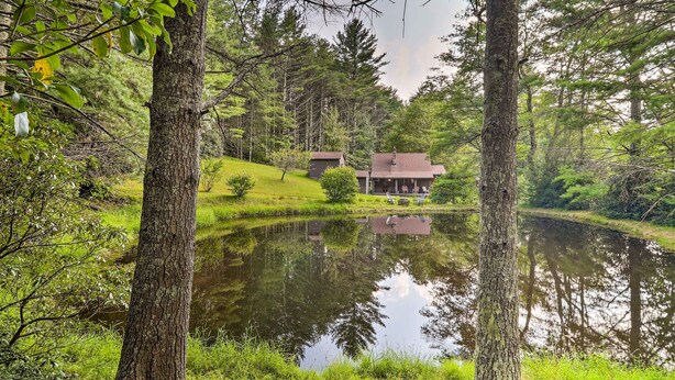 A cabin with a pond in front, surrounded by trees and greenery. - Rustic Cabin w/ Patio & Pond on Blue Ridge Parkway (Ennice)
