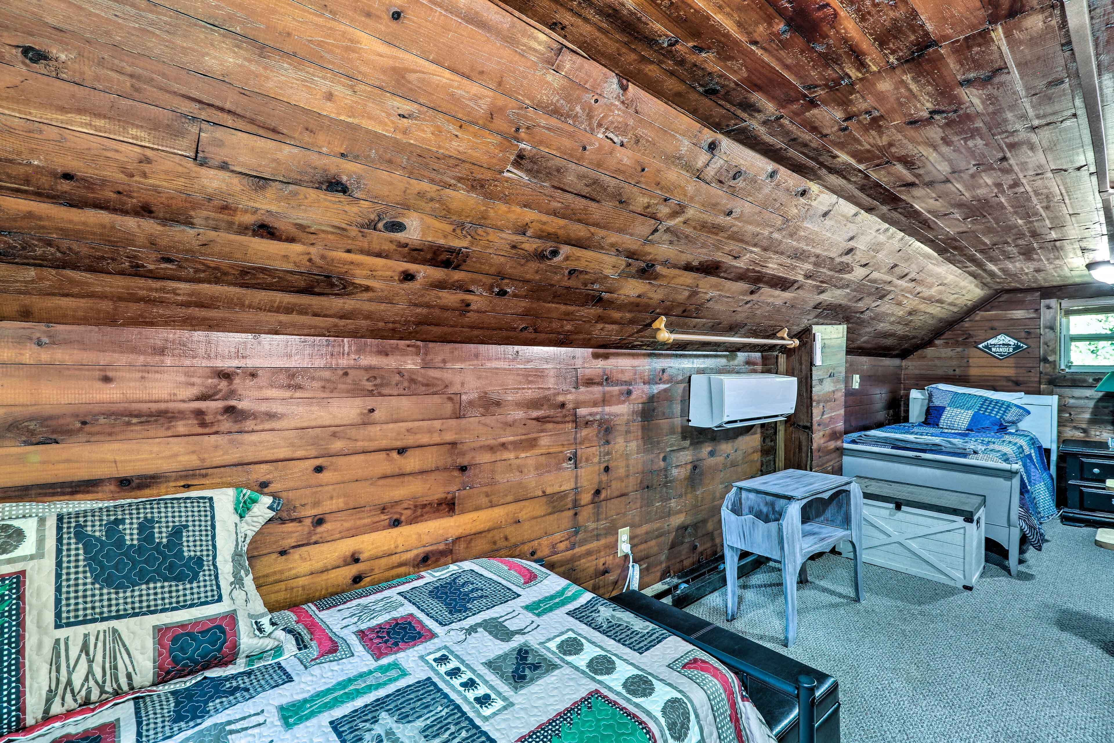 A cozy cabin room with a wooden ceiling, a bed with a quilt, a desk, and a chair.