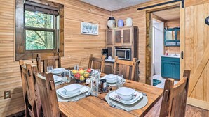 A wooden dining room with a table set for four, a window, and a kitchen area visible through an open door. - Rustic Cabin w/ Patio & Pond on Blue Ridge Parkway (Ennice)