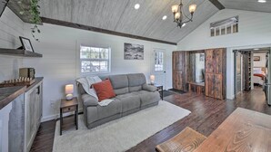 A spacious living area with a gray sofa, wooden flooring, and a chandelier. - Contemporary Cabin w/ Mountain Views & Deck (Bonners Ferry)