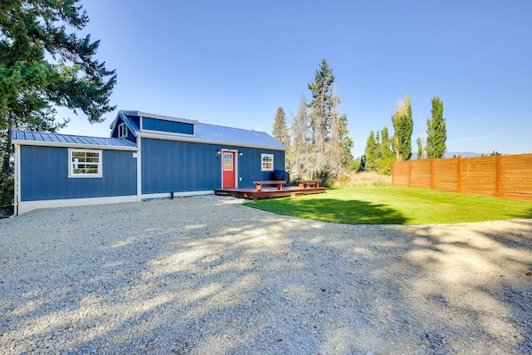 A blue building with a red door, a gravel driveway, and a wooden fence.