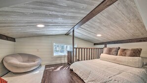 A bedroom with a sloped ceiling, a bed with a patterned bedspread, a chair, and a window. - Contemporary Cabin w/ Mountain Views & Deck (Bonners Ferry)