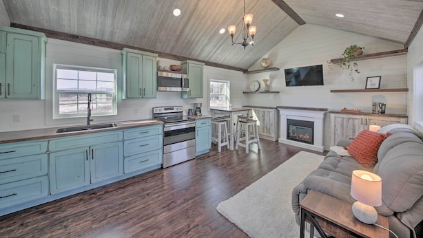 A spacious kitchen with light blue cabinets, a large island, and a dining area with a fireplace. - Contemporary Cabin w/ Mountain Views & Deck (Bonners Ferry)