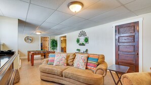 A living room with a beige sofa, a wooden coffee table, and a door with a decorative panel. - Cozy Historic Home w/ Games, Near Bryce Canyon! (Cannonville)