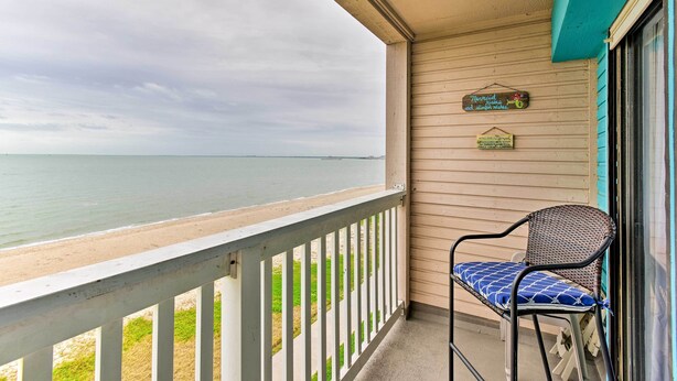 A balcony with a view of the beach and ocean, a wicker chair with a cushion, and a sign indicating a restaurant.