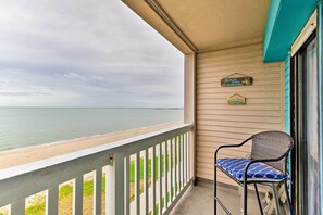 A balcony with a view of the beach and ocean, a wicker chair with a cushion, and a sign indicating a restaurant.