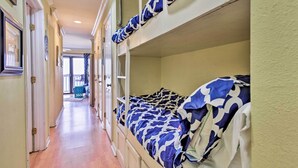 A narrow hallway with wooden flooring and bunk beds with blue and white patterned bedding.