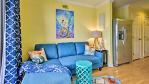 A living room with a blue sofa, a teal side table, and a painting of a mermaid on the wall.