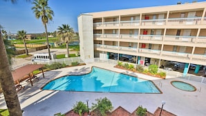 A multi-story hotel with a swimming pool, outdoor seating, and palm trees.