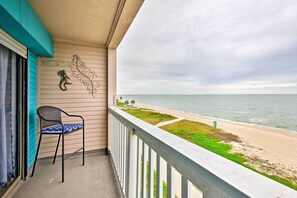 A balcony with a chair, a decorative seahorse, and a view of the beach and ocean.