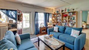 A living room with a blue sofa, a coffee table, and a bookshelf filled with books and decorative items. - Eclectic Manitowoc Vacation Rental Near Marina! (Manitowoc)