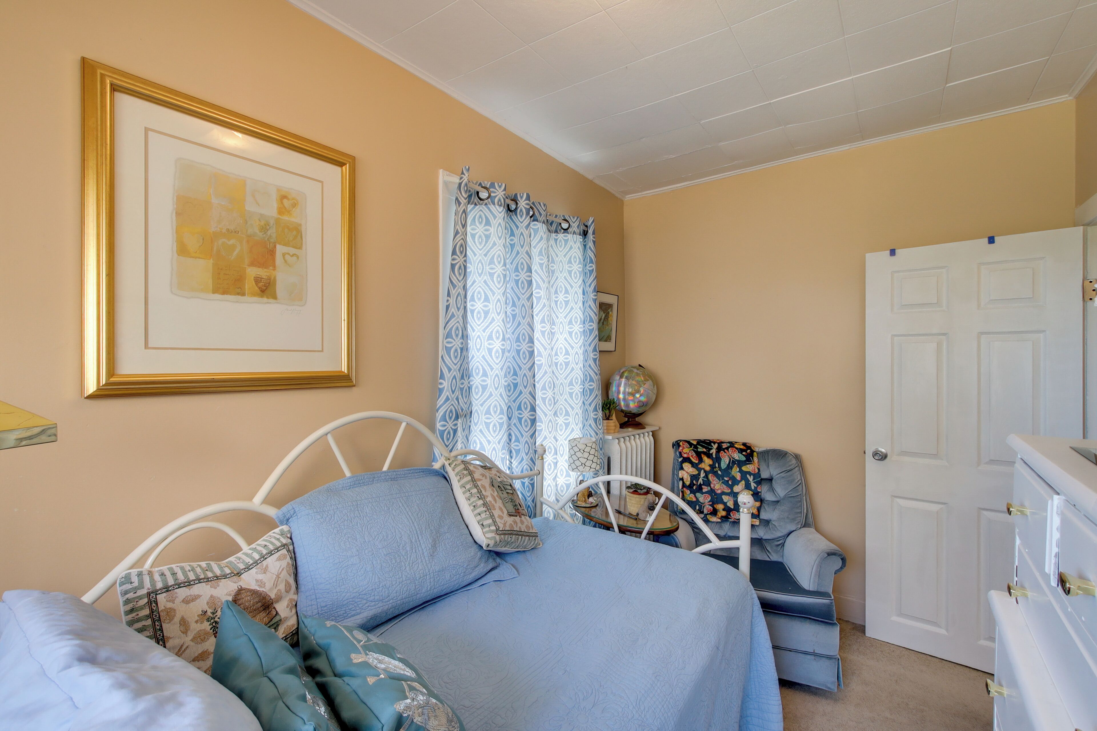 A bedroom with a bed, a chair, a dresser, a framed picture on the wall, and a door.