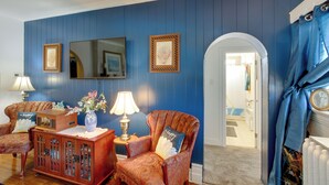 A room with blue walls, a wooden cabinet, two patterned armchairs, a television, and a mirror. - Eclectic Manitowoc Vacation Rental Near Marina! (Manitowoc)