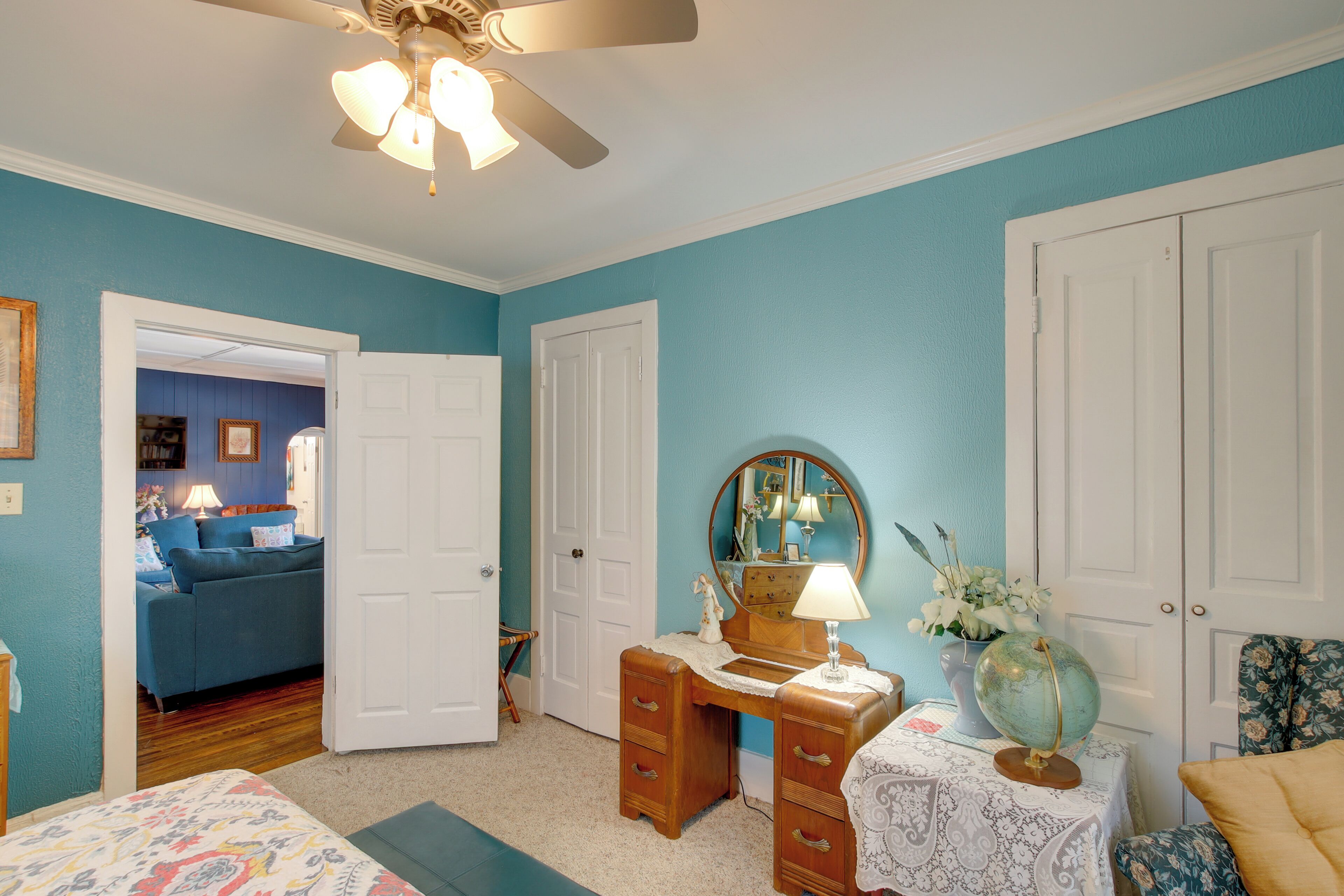 A bedroom with a bed, a dresser, a vanity with a mirror, a globe, and a chair.