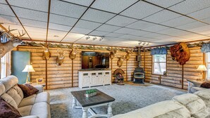A log cabin interior with a fireplace, mounted animal heads, a television, and a cozy seating area. - Cozy Cass City Retreat w/ Spacious Deck! (Cass City)