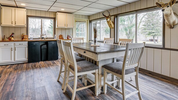 A dining area with a wooden table and chairs, a kitchen with white cabinets, and a mounted deer head on the wall. - Cozy Cass City Retreat w/ Spacious Deck! (Cass City)