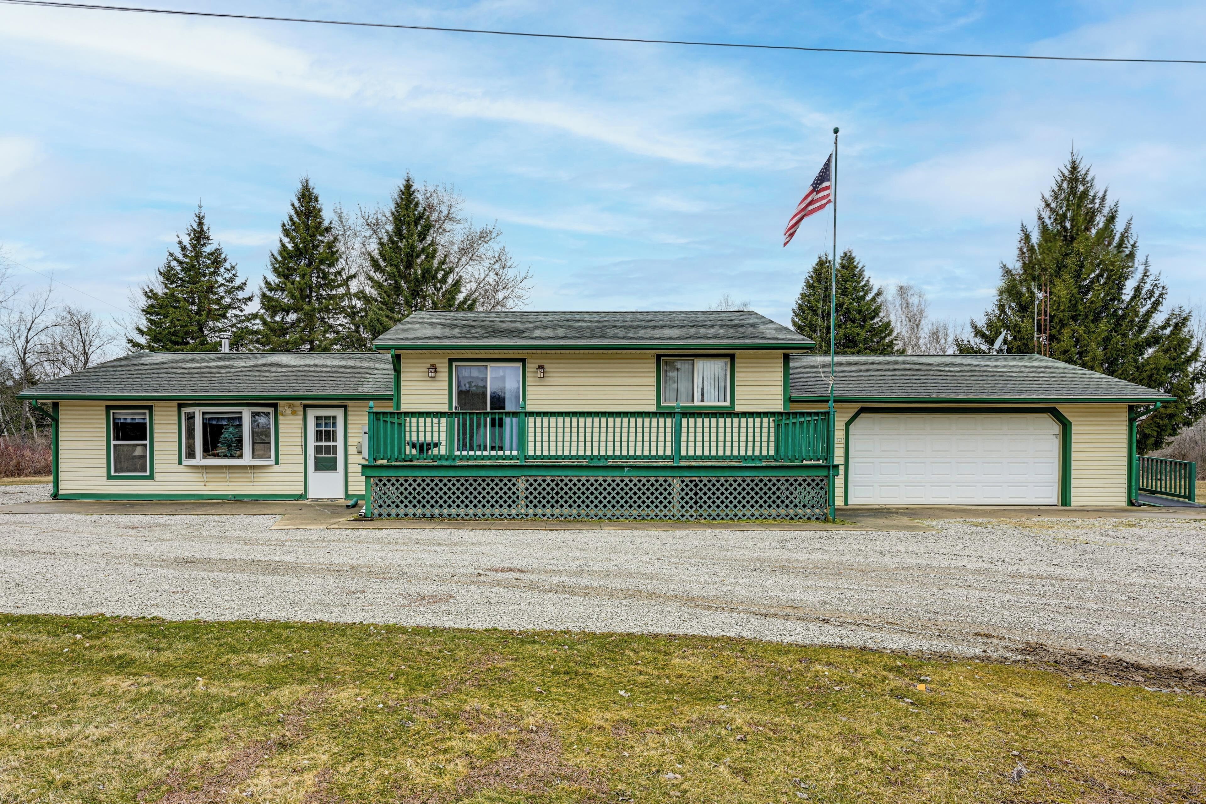 A two-story house with a green porch, a garage, and a flagpole with an American flag.