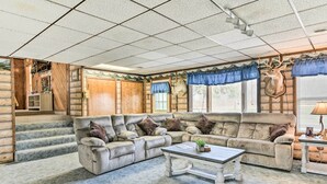 A log cabin interior with a large L-shaped sectional sofa, a coffee table, and a staircase leading to an upper level. - Cozy Cass City Retreat w/ Spacious Deck! (Cass City)