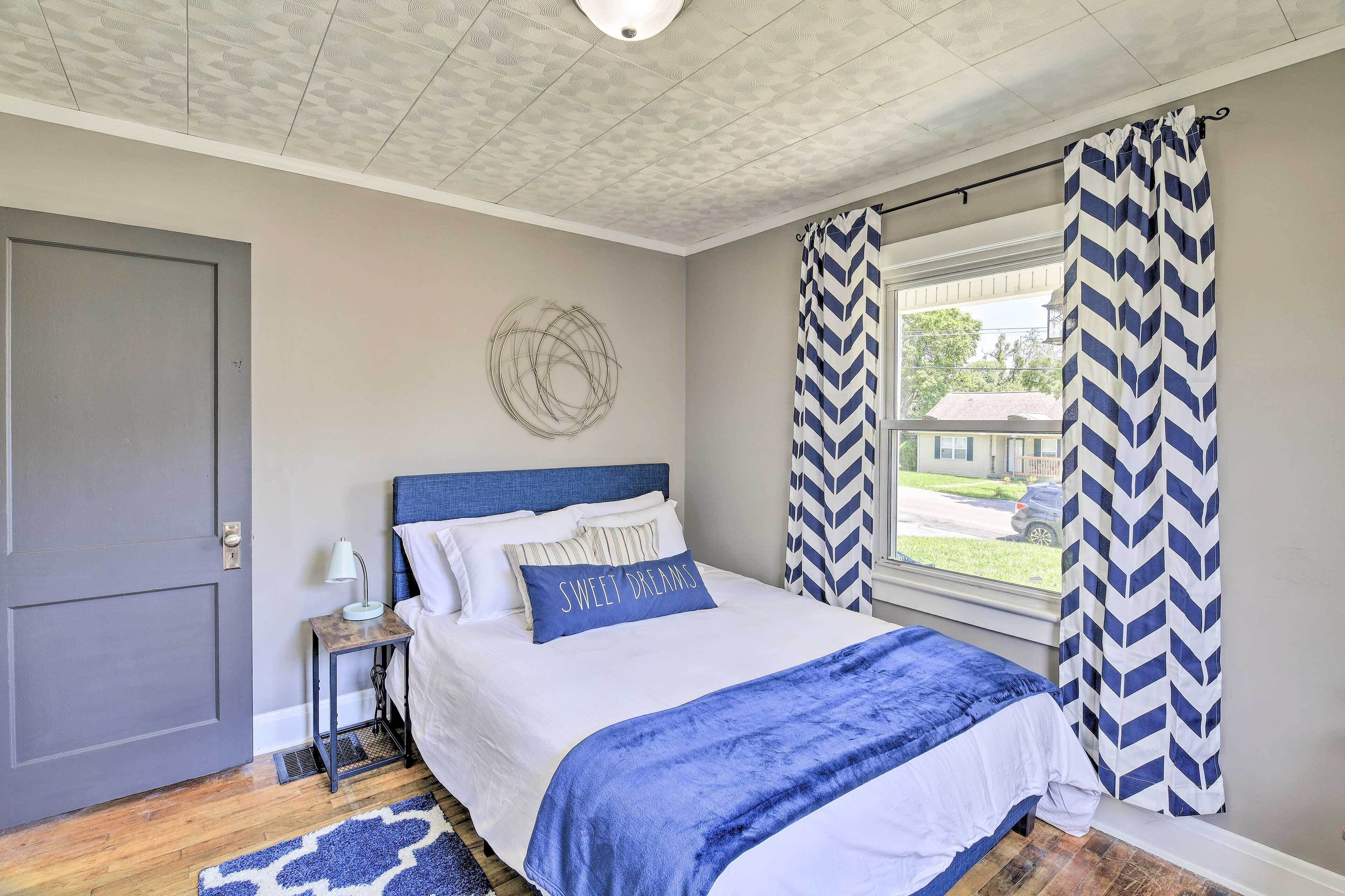 A bedroom with a bed, a nightstand, a window with curtains, and a door.
