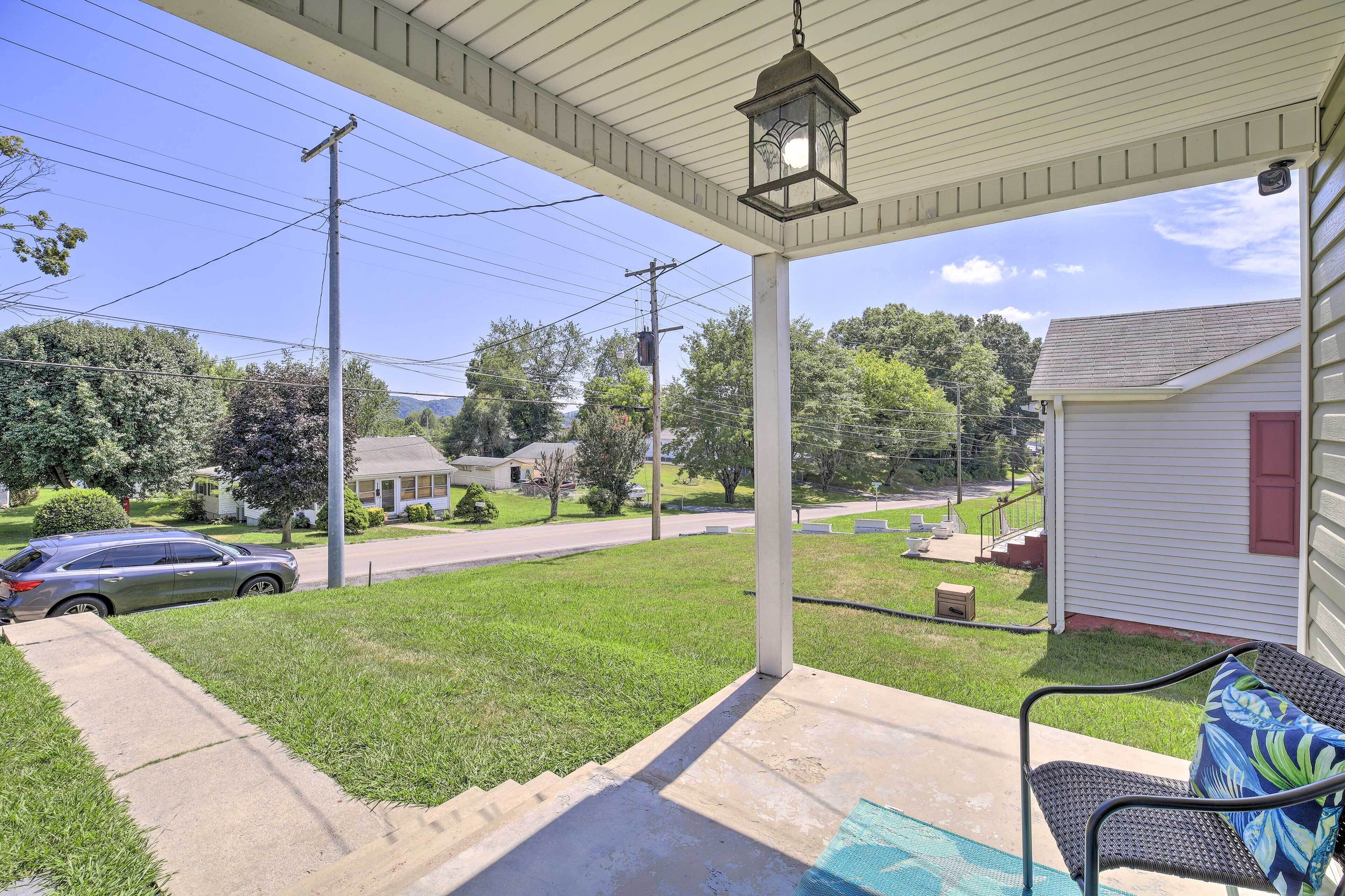 A covered porch with a bench and a lantern, overlooking a residential street with houses and a car.