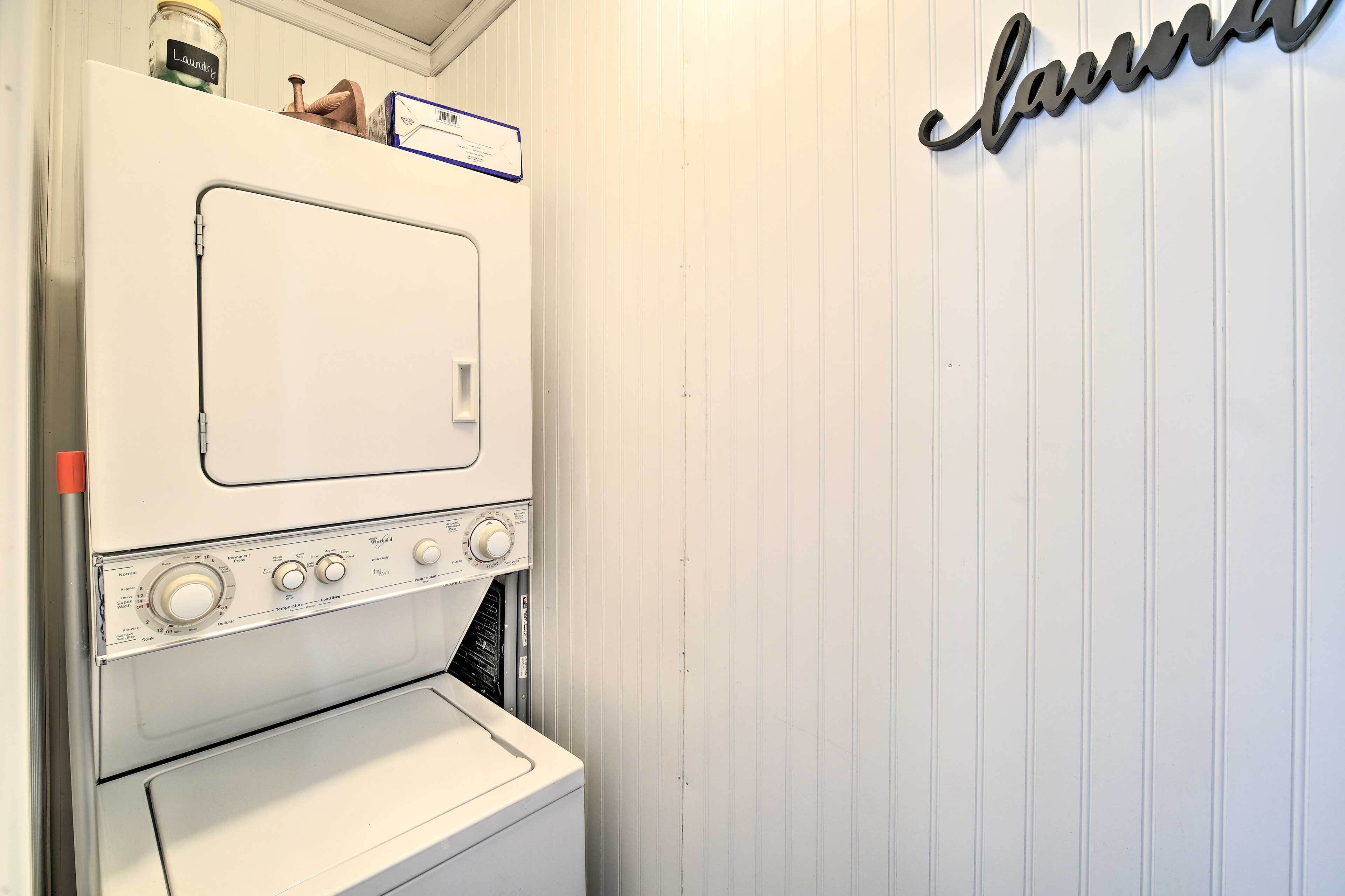 A laundry room with a white Whirlpool washer and dryer, a shelf with a jar labeled 'Laundry,' and a wall-mounted sign spelling 'laundromat.'