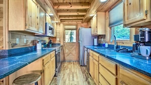 A compact kitchen with wooden cabinets, a central island, and a window providing natural light. - Family-friendly Gatlinburg Cabin w/ Pool Access! (Gatlinburg)