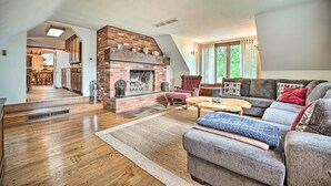 Ein geräumiges Wohnzimmer mit Kamin aus Backsteinen, einem großen Sofa und einem Essbereich, der durch einen offenen Bogen zu sehen ist.