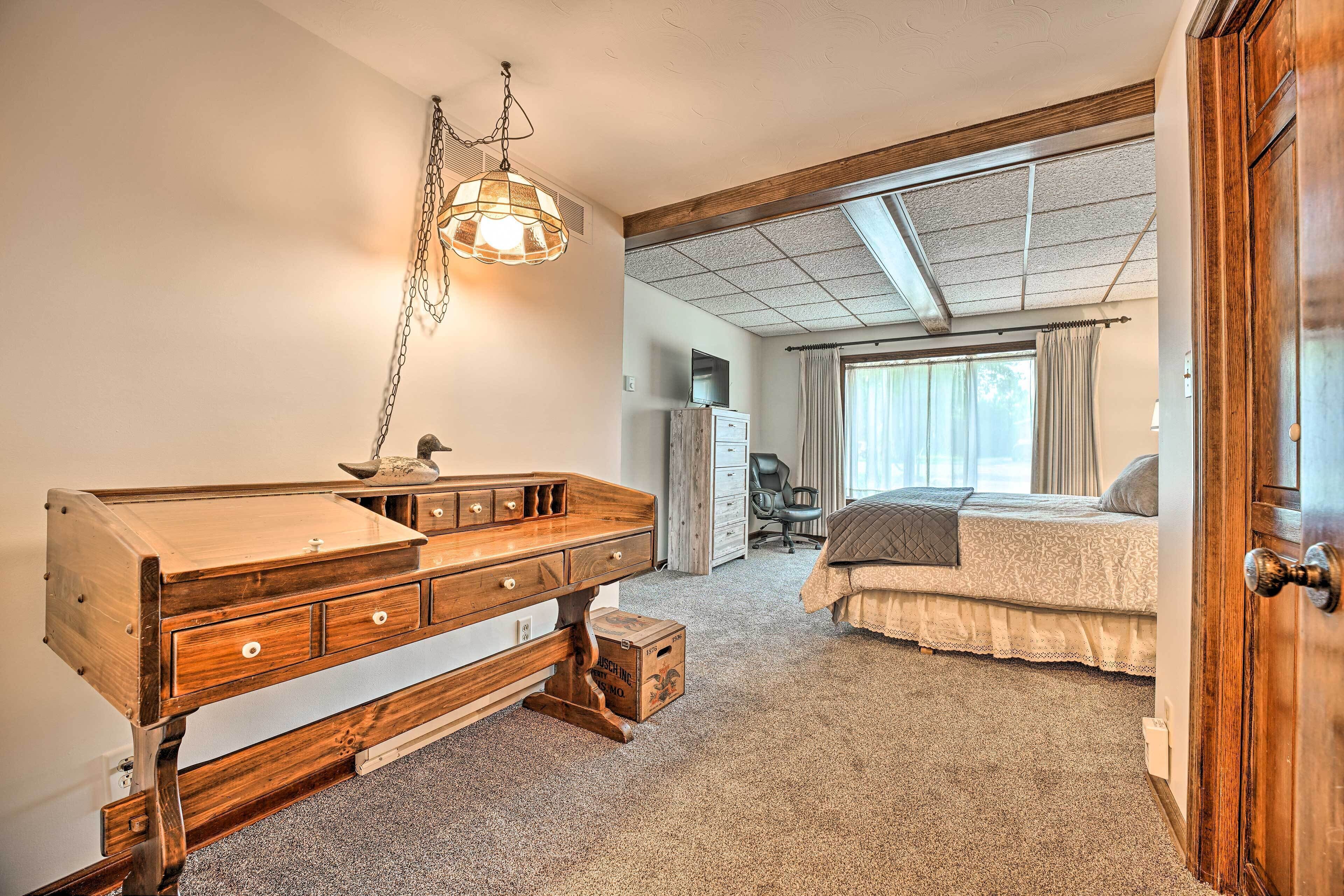 A bedroom with a wooden desk, a bed, and a large window.