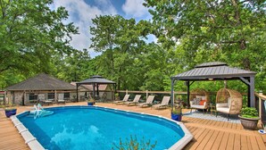 Une piscine avec une terrasse en bois, des chaises longues et un kiosque.