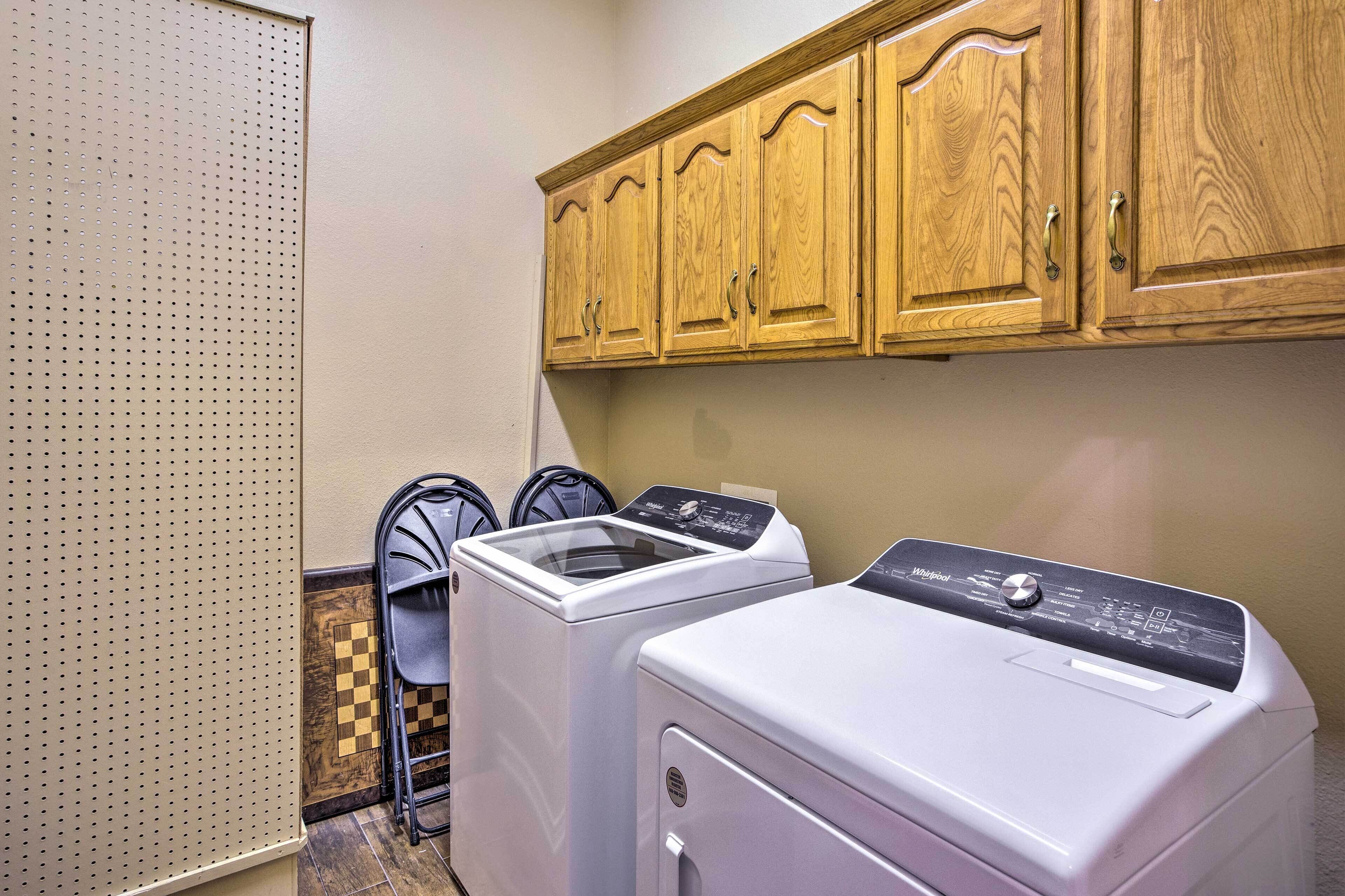 A laundry room with two front-loading washing machines, wooden cabinets above, and a folding chair.