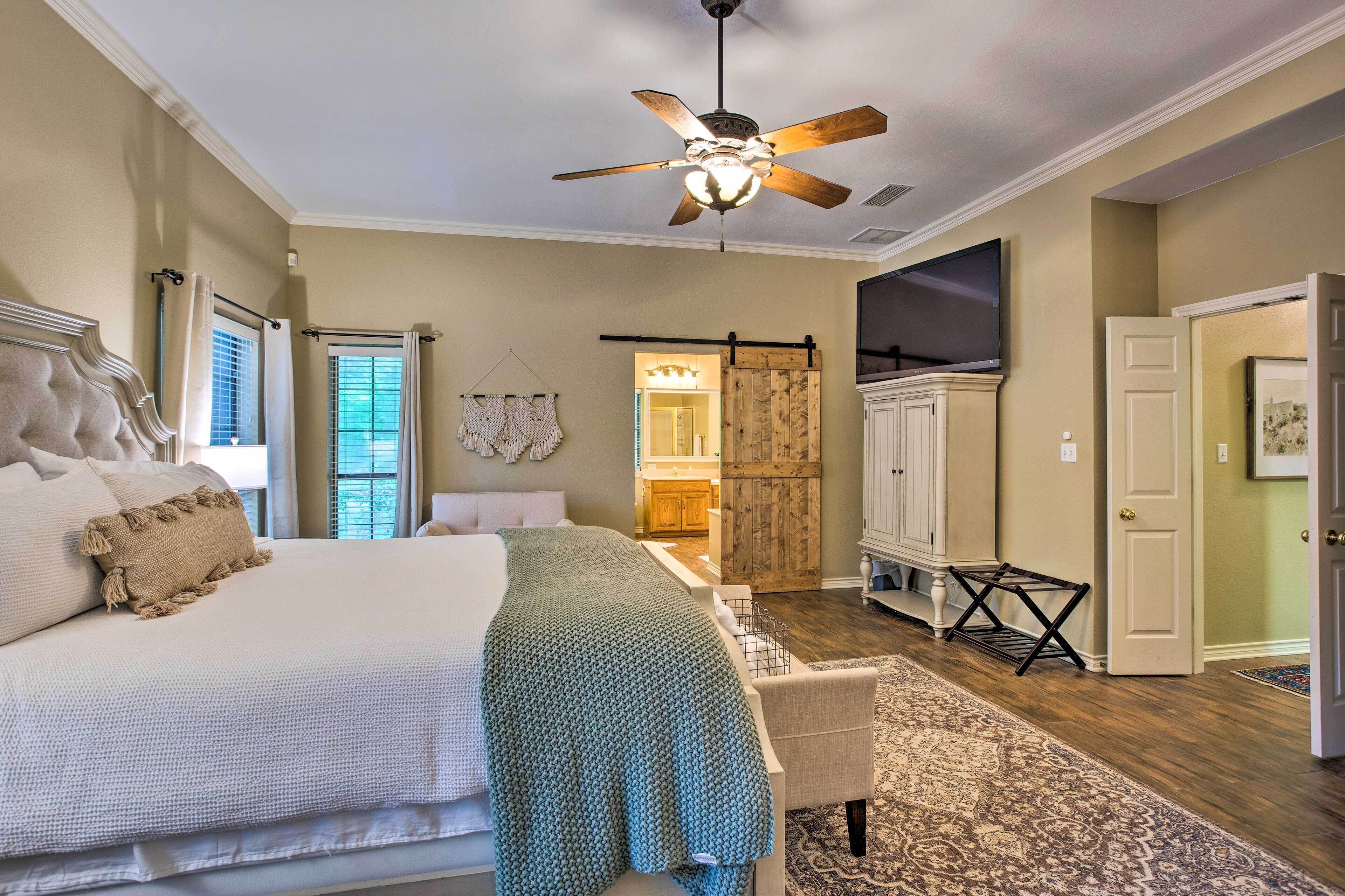 A bedroom with a bed, a ceiling fan, a large window, and a door leading to another room.