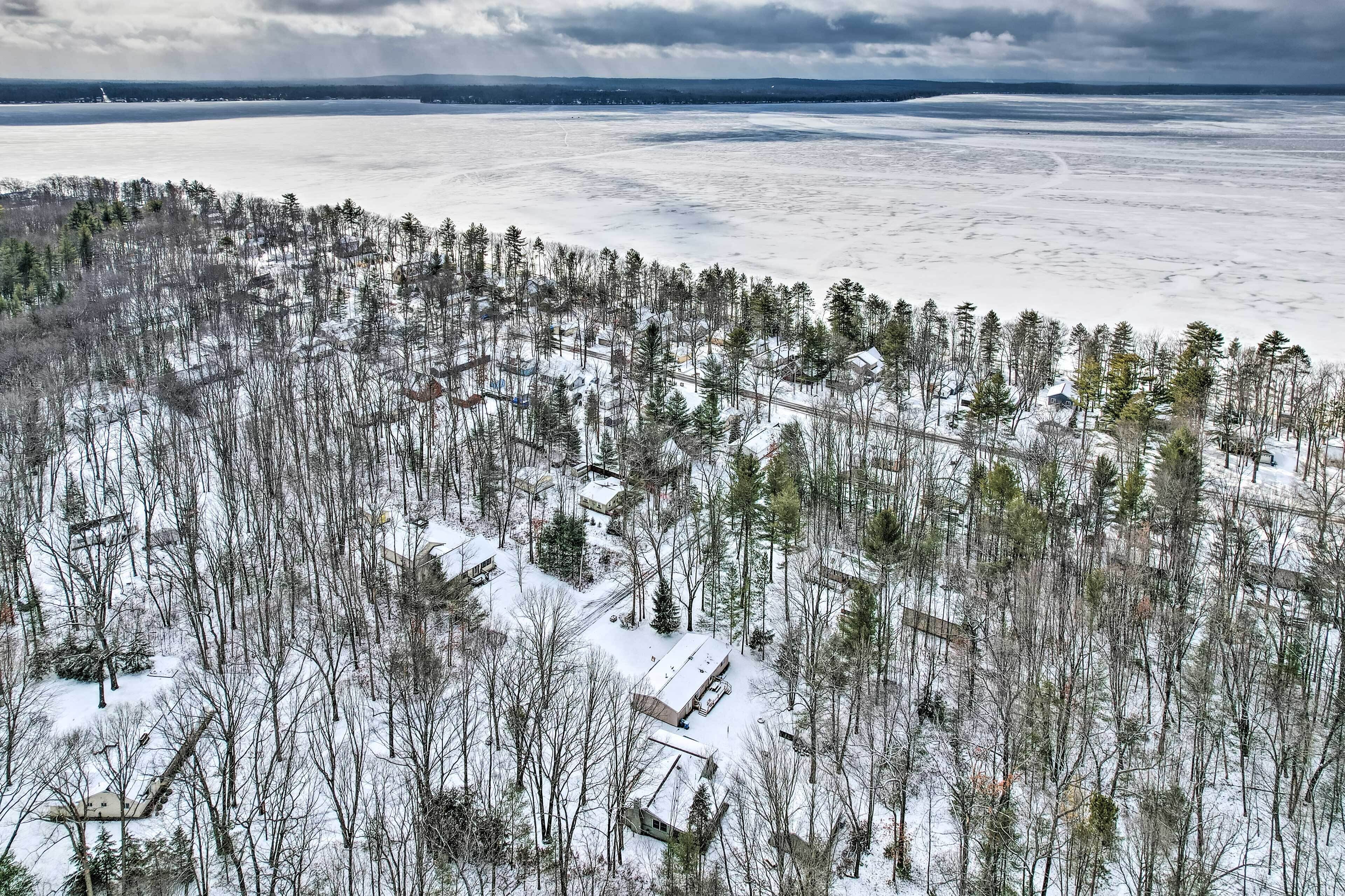 Une vue aérienne d’une forêt enneigée avec plusieurs bâtiments, dont une grande maison et de plus petites cabanes, le tout entouré d’arbres.