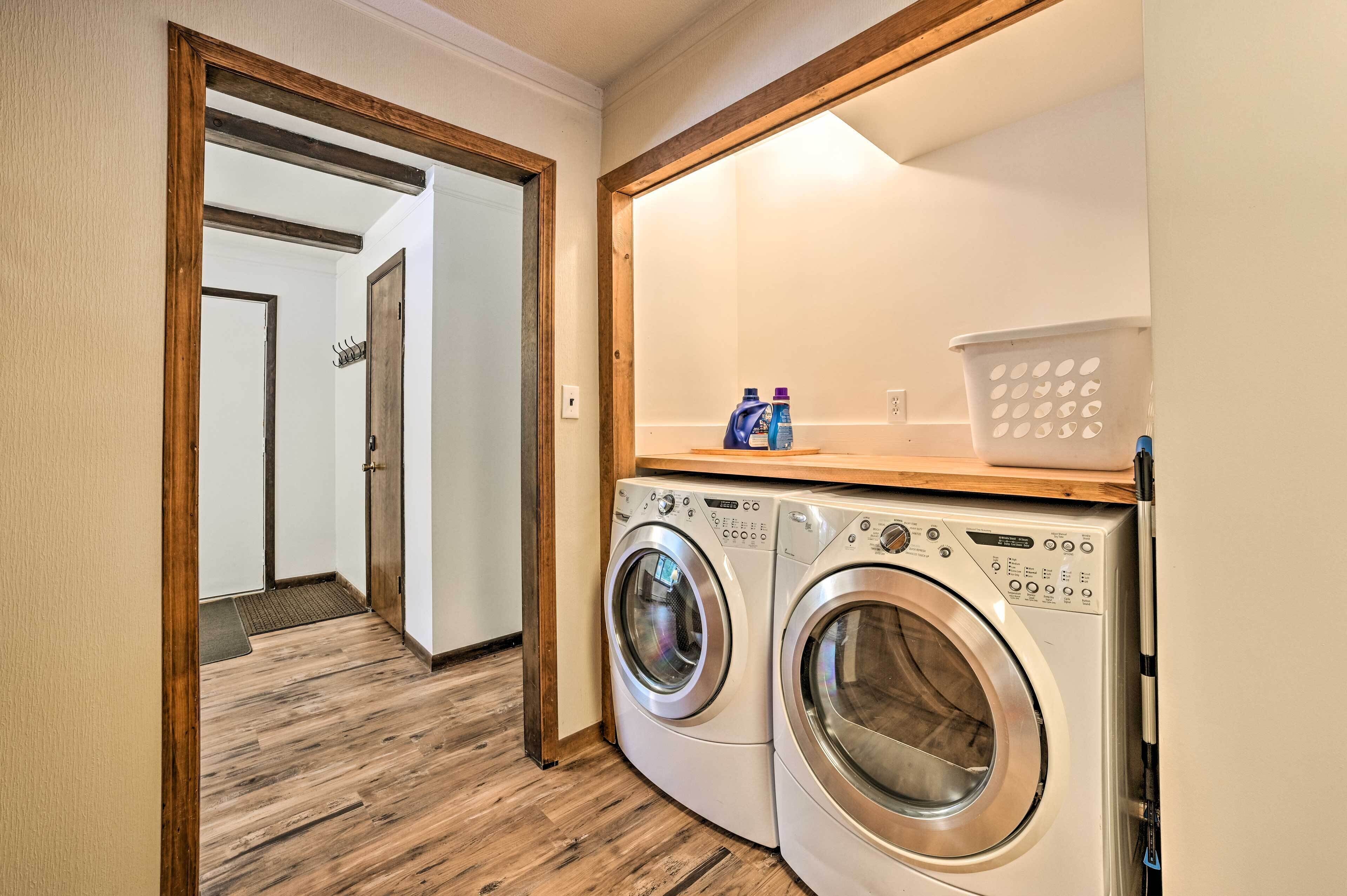 A laundry area with two front-loading washing machines, a wooden shelf with a laundry basket, and a door leading to another room.
