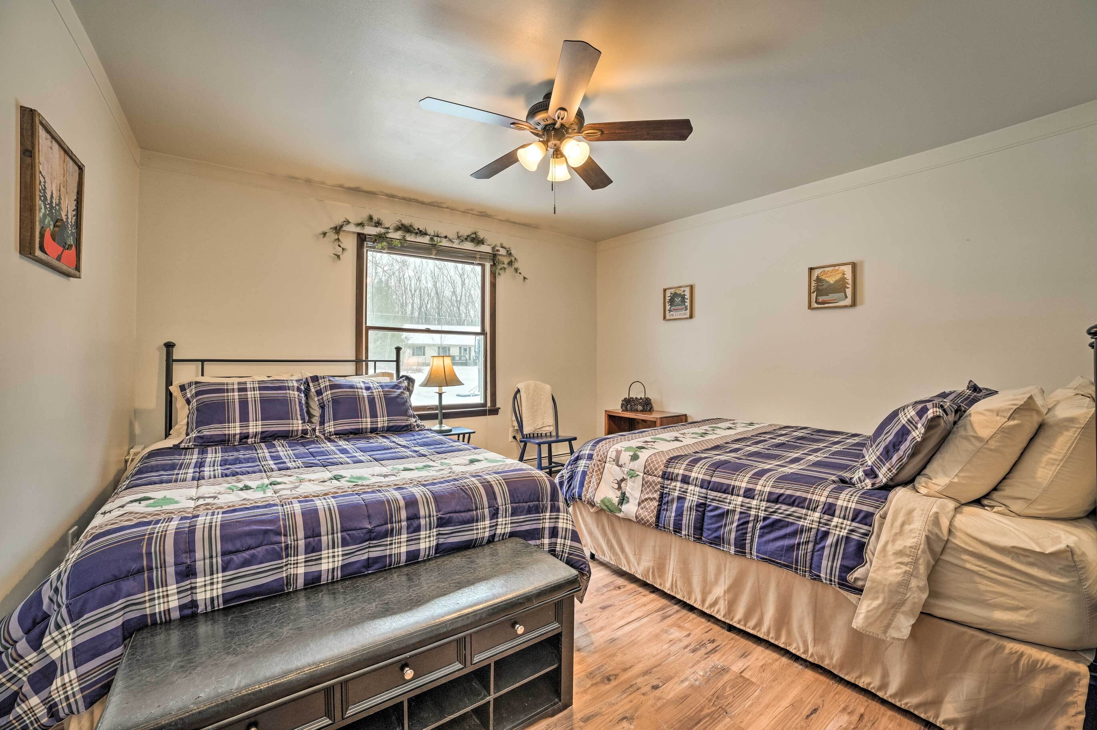 A bedroom with two beds, a ceiling fan, a window with a view, and a bench.