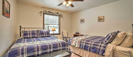 A bedroom with two beds, a ceiling fan, a window with a view, and a bench.