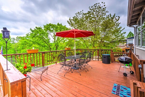 A wooden deck with a table and chairs, a red umbrella, and a barbecue grill.