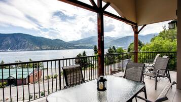 A balcony with a glass table, chairs, and a lantern. It overlooks a lake and mountains.