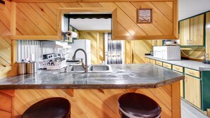 A kitchen with wooden walls, a marble countertop, a sink, and two stools. - Burkesville Vacation Rental - 5 Mi to the Lake! (Burkesville)