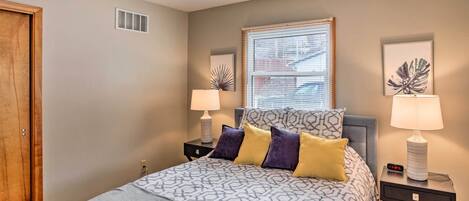 A bedroom with a bed, two bedside tables, a ceiling fan, a window with blinds, and a door.
